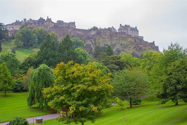 Edinburgh Castle on a rocky hill surrounded by lush green trees under a grey sky