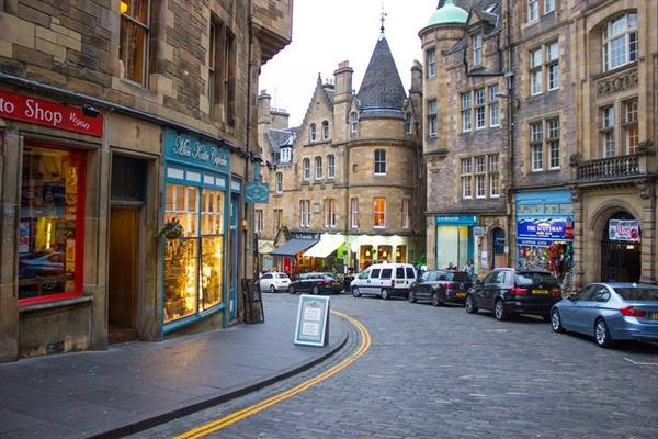 Cockburn Street in Edinburgh, stone buildings, lit shopfronts and parked cars