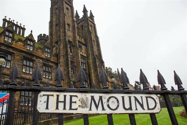 The Mound sign on black iron railings before a Gothic stone building in Edinburgh