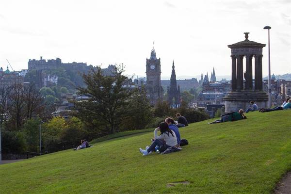 People resting on Calton Hill's grass, Edinburgh, beside the Dugald Stewart Monument