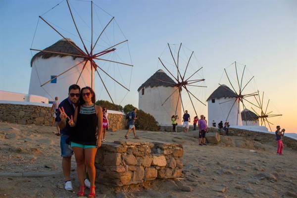 Tourists pose before the famous windmills of Mykonos at dusk