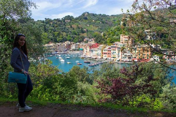 Smiling woman with turquoise bag on hillside trail above Portofino harbor