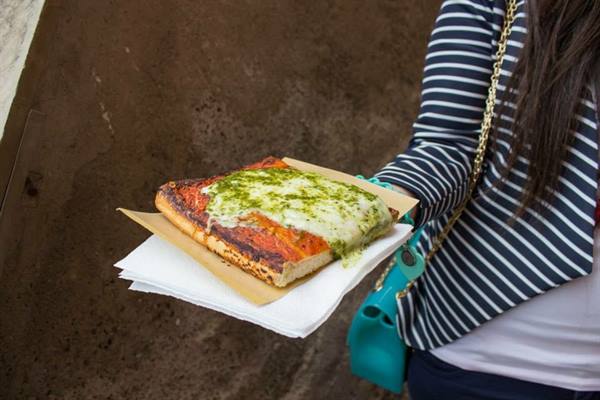 Woman in striped top with turquoise bag holds pesto focaccia on a napkin