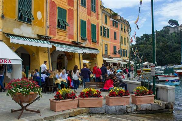 Tourists at café tables on Portofino harbor among colorful houses and flowers