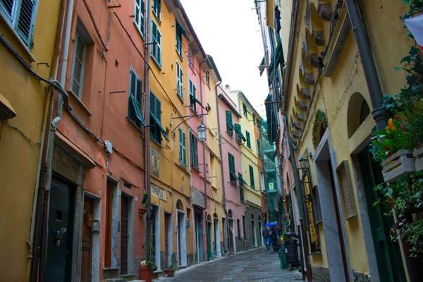Narrow alley between pastel houses with green shutters, wet cobblestones in Monterosso