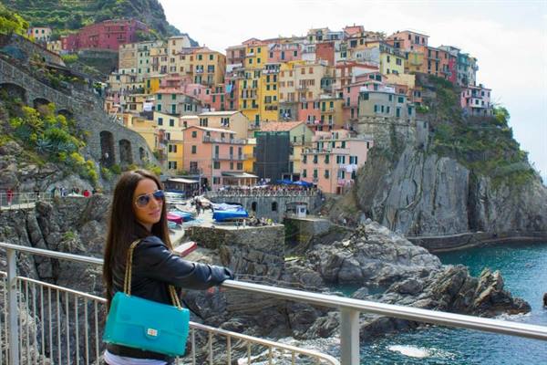 Tourist with turquoise bag in front of Manarola's colorful houses by the sea