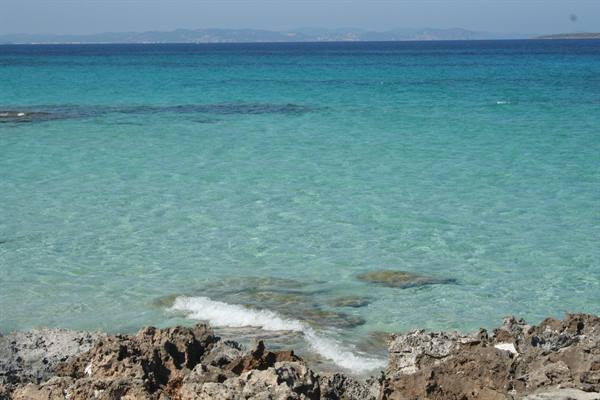 Turquoise clear water over limestone rocks, foam among stones, distant coastline