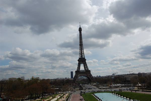 The wrought-iron Eiffel Tower under grey clouds, gardens and fountain below