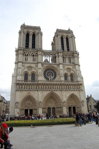 Gothic facade of Notre-Dame in Paris, tourists queuing under grey sky