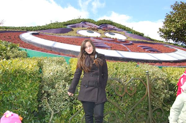 Woman in black coat by green hedge in front of Disney's Cheshire Cat garden