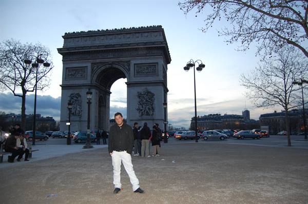 Tourist posing in front of the Arc de Triomphe in Paris at dusk
