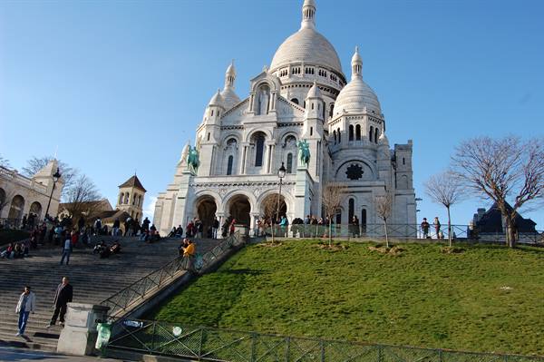 Tourists on stairs and lawn before the white Sacré-Cœur basilica in Montmartre