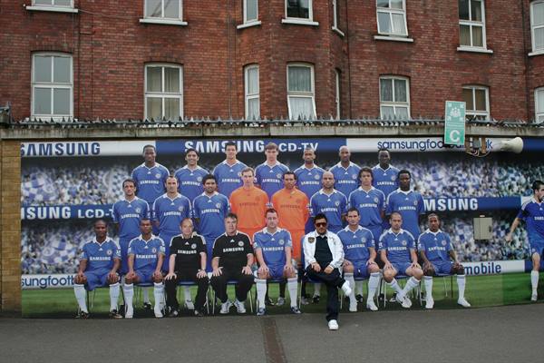 Chelsea players in blue kits pose in front of Samsung banner on brick wall