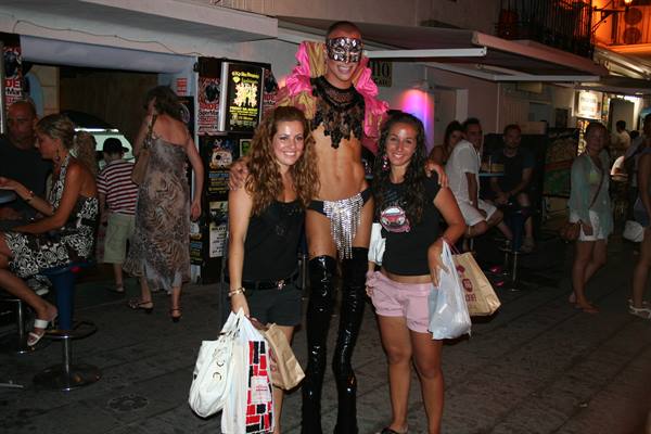 Two tourists with shopping bags next to a sequined drag queen in black boots