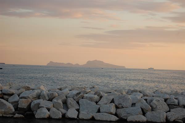 White breakwater rocks before the sea, Capri island fading in evening light