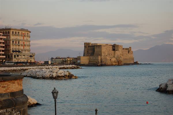 Castel dell'Ovo in Naples, calm sea, rocks and brick buildings