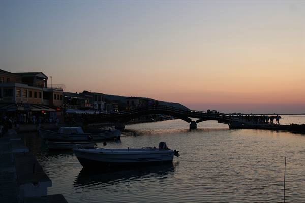Boats moored at Lefkada harbor at dusk, wooden bridge over water