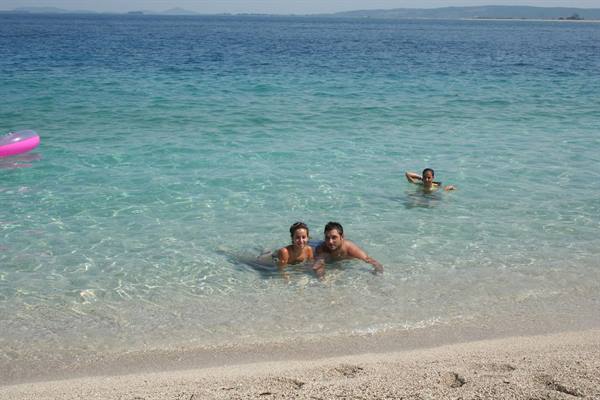 Couple swims in clear turquoise water, pink float left, sandy beach