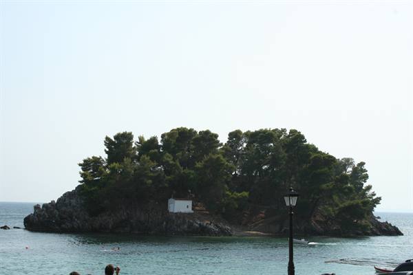 Chapel on a pine-covered islet, swimmer in the water, lamppost in foreground
