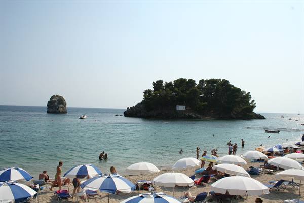 Parga beach with white umbrellas, swimmers and a green islet