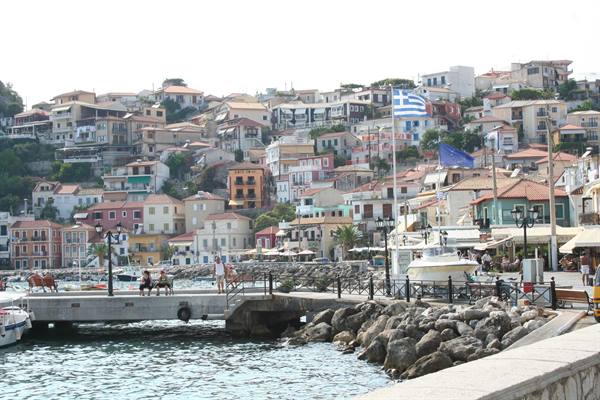 Greek flag on Parga's pier, colorful hillside houses, stone waterfront promenade
