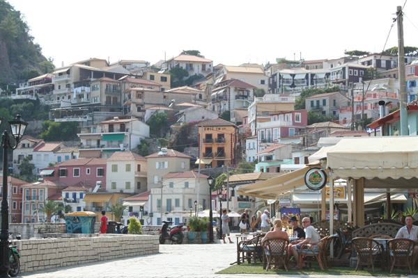 People at café tables beneath Parga's colorful hillside houses
