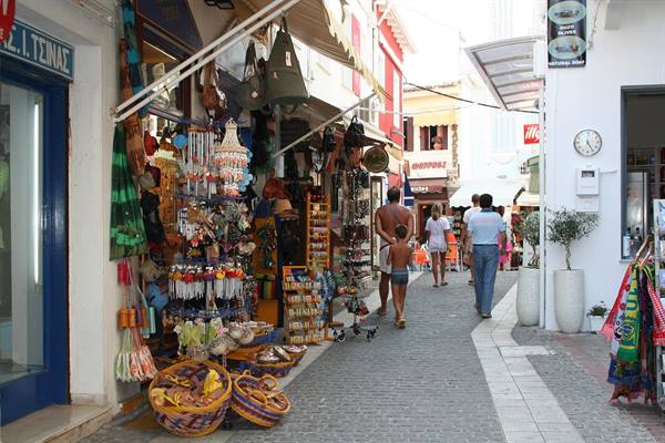 Tourists walk past souvenir shops and woven baskets in a narrow street