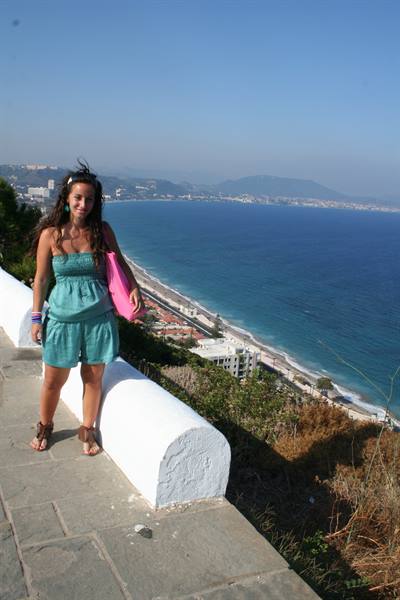 Woman in green outfit by white wall above Almuñécar coastline