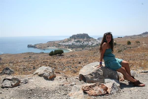 Girl sitting on a rock, behind Lindos bay and acropolis