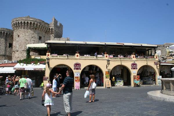 Tourists stroll past arched shops beneath ancient medieval stone towers