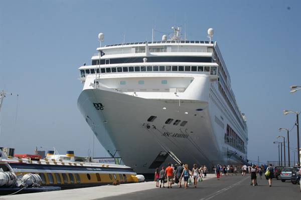 Tourists walk along the pier beside the docked MSC Lirica cruise ship