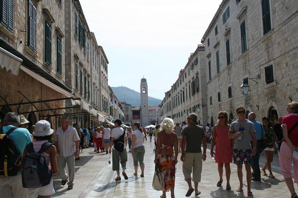 Tourists walk along Stradun, the polished limestone street with Dubrovnik bell tower