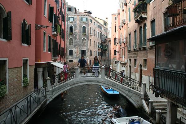 Tourists on a stone bridge in Venice, colorful houses and boats on the canal