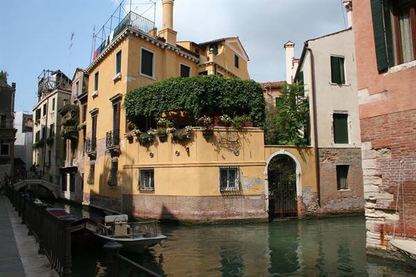 Yellow ivy-covered house with flowers along a Venice canal