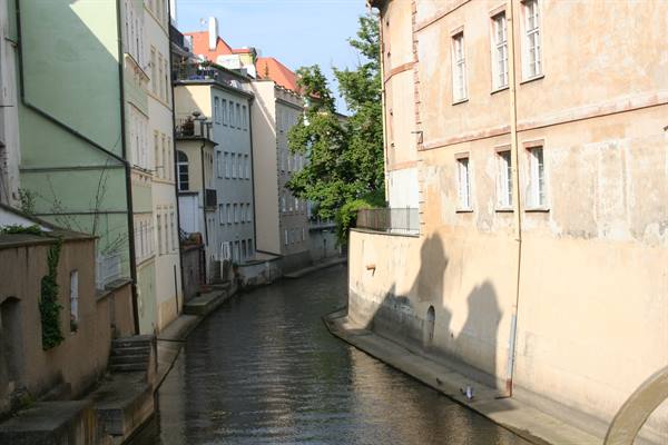 Narrow canal between pastel facades in Prague, sunlight and shadow on ochre wall