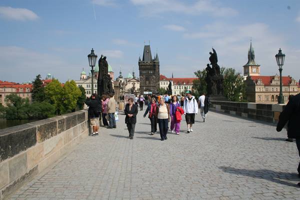 Tourists walk on Charles Bridge among statues and Gothic towers in Prague