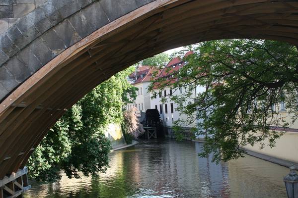 Under the stone bridge arch, a canal with wooden waterwheel and houses