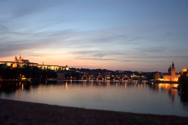 Prague Castle and Charles Bridge lights reflect on the Vltava at dusk