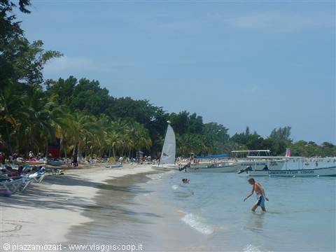 Sandy beach with palm trees, fishing boats moored and tourists swimming