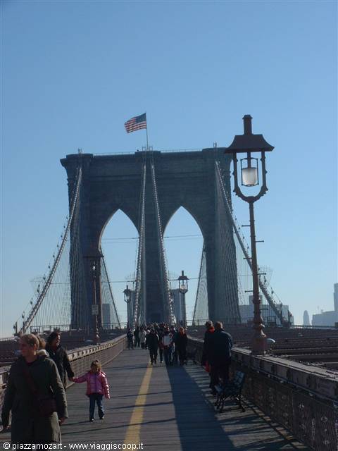 Pedestrians on Brooklyn Bridge under gothic stone tower with American flag