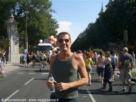 Man in tank top and sunglasses smiling on a crowded street, likely Madrid, Retiro