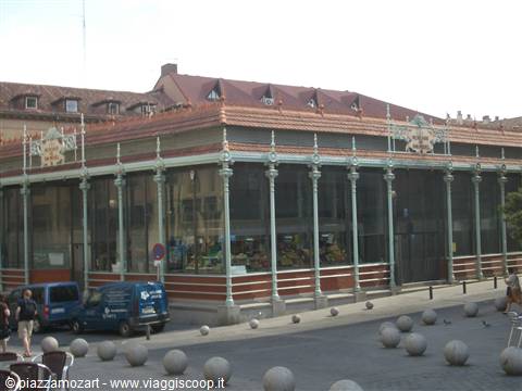 Cast-iron glass market hall with red roof, stone bollards on the square