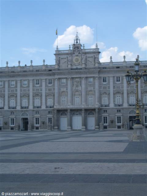 Stone facade of the Royal Palace of Madrid under cloudy sky, lampposts nearby
