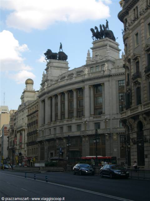 Gran Vía in Madrid, stone building with bronze horse chariots, cars passing by