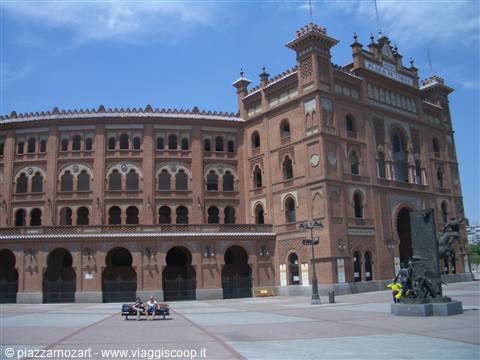 Red-brick bullring with arches and towers under blue sky