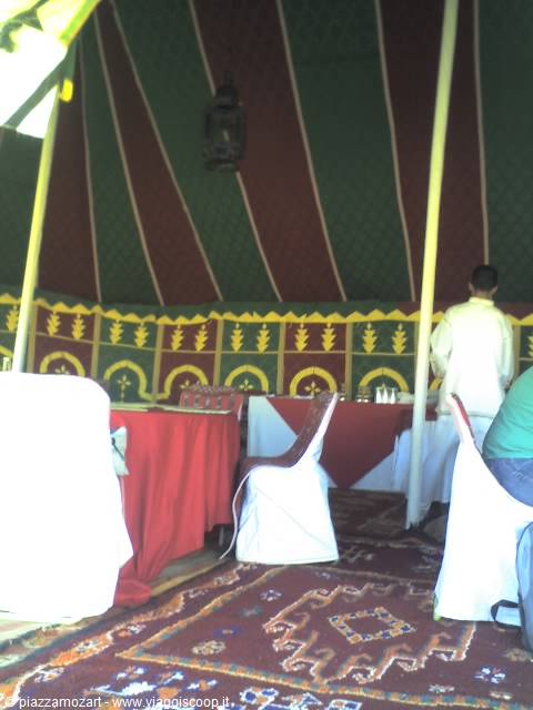Inside a decorated tent with red carpets, set tables and a waiter