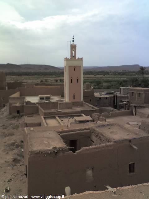 Pink minaret rising among mud-brick houses in Taouz kasbah under cloudy sky