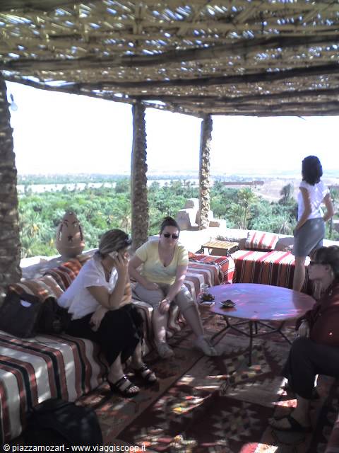 Women seated on striped sofas under cane pergola, palm grove in background