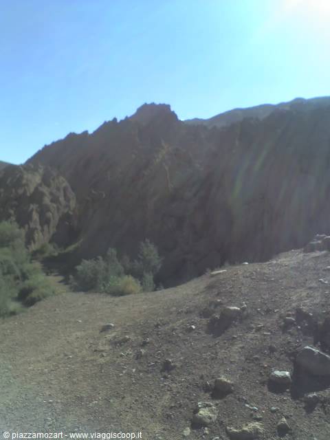 Sunlit rocky crags above a stony trail with green shrubs