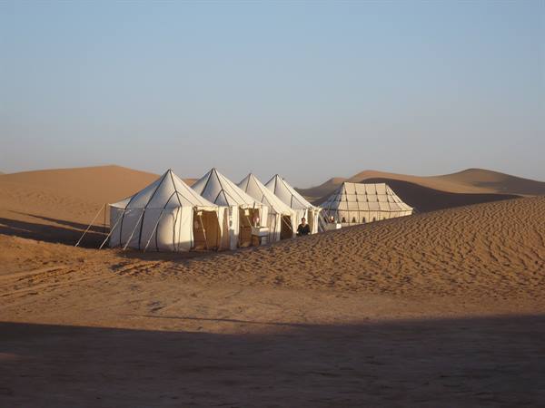 White canvas tents among sand dunes in warm morning light